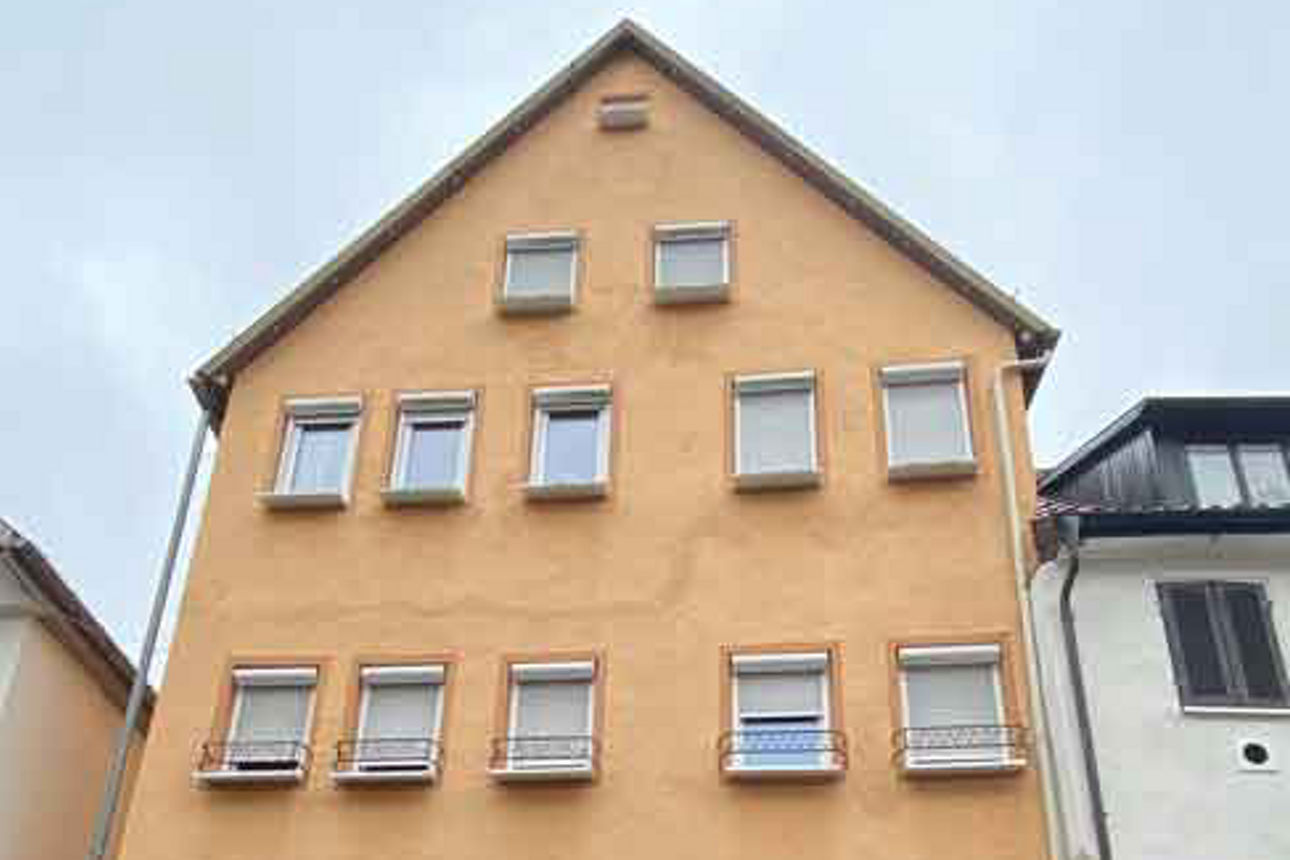 Ein Wohn- und Geschäftshaus in der Außenansicht. Es ist orange gestrichen.