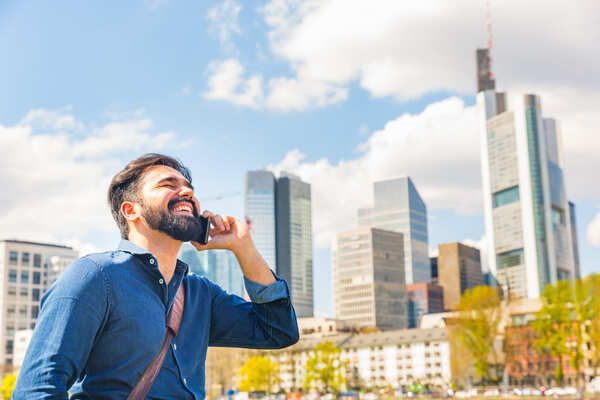 Ein junger Mann telefoniert lachend vor der Skyline von Frankfurt