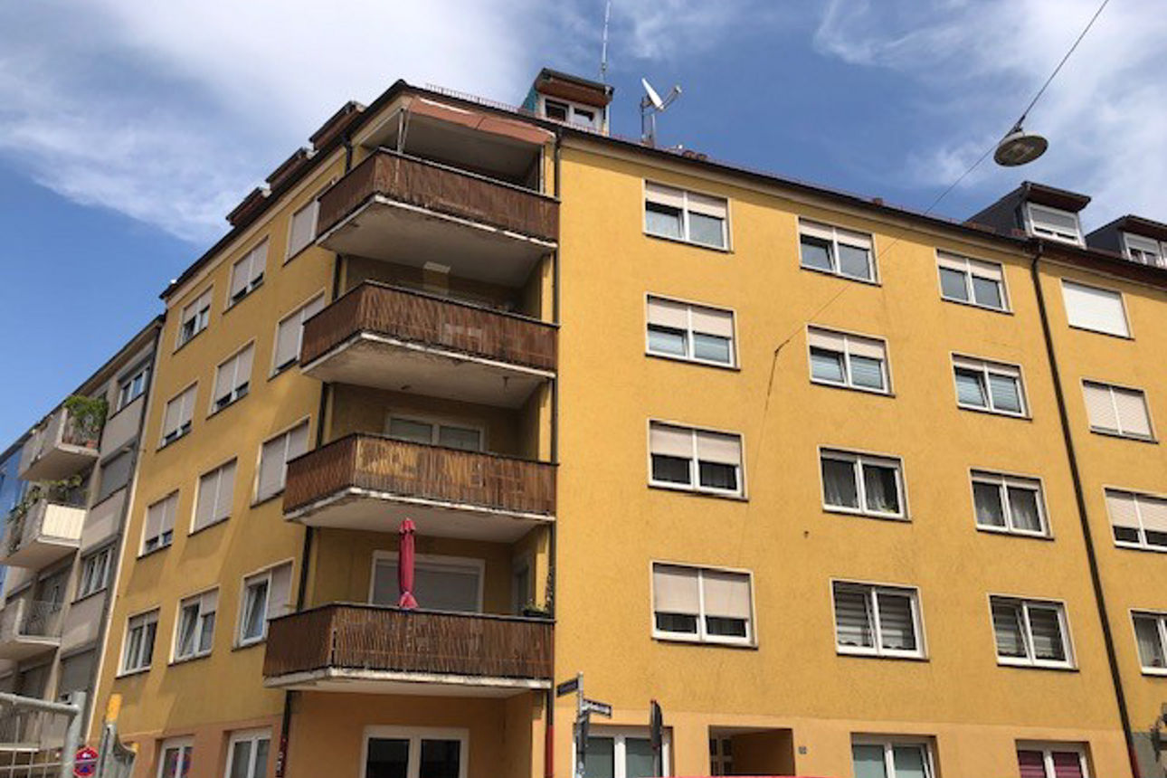 Bild zeigt ein mehrstöckiges Wohnhaus mit gelber Fassade, Holz-Balkonen in einer städtischen Umgebung.