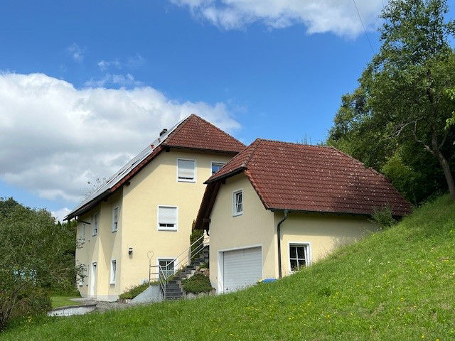 Gelbes Haus in Hanglage, rotes Dach, Grünfläche im Vordergrund