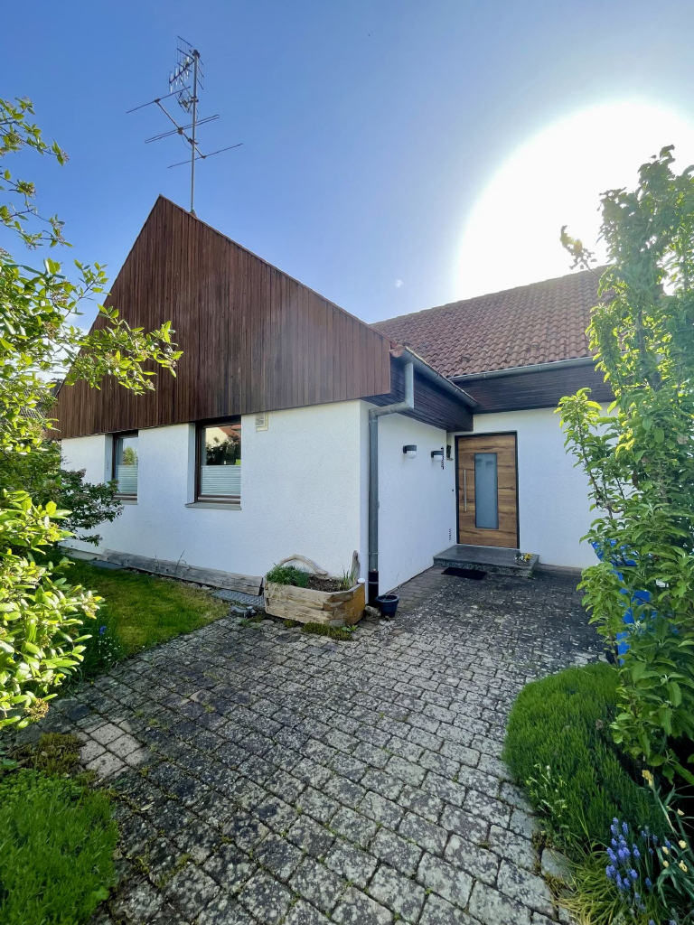 Bild von weißem Einfamilienhaus mit Holzverkleidung an Fassade und gepflastertem Zugangsbereich