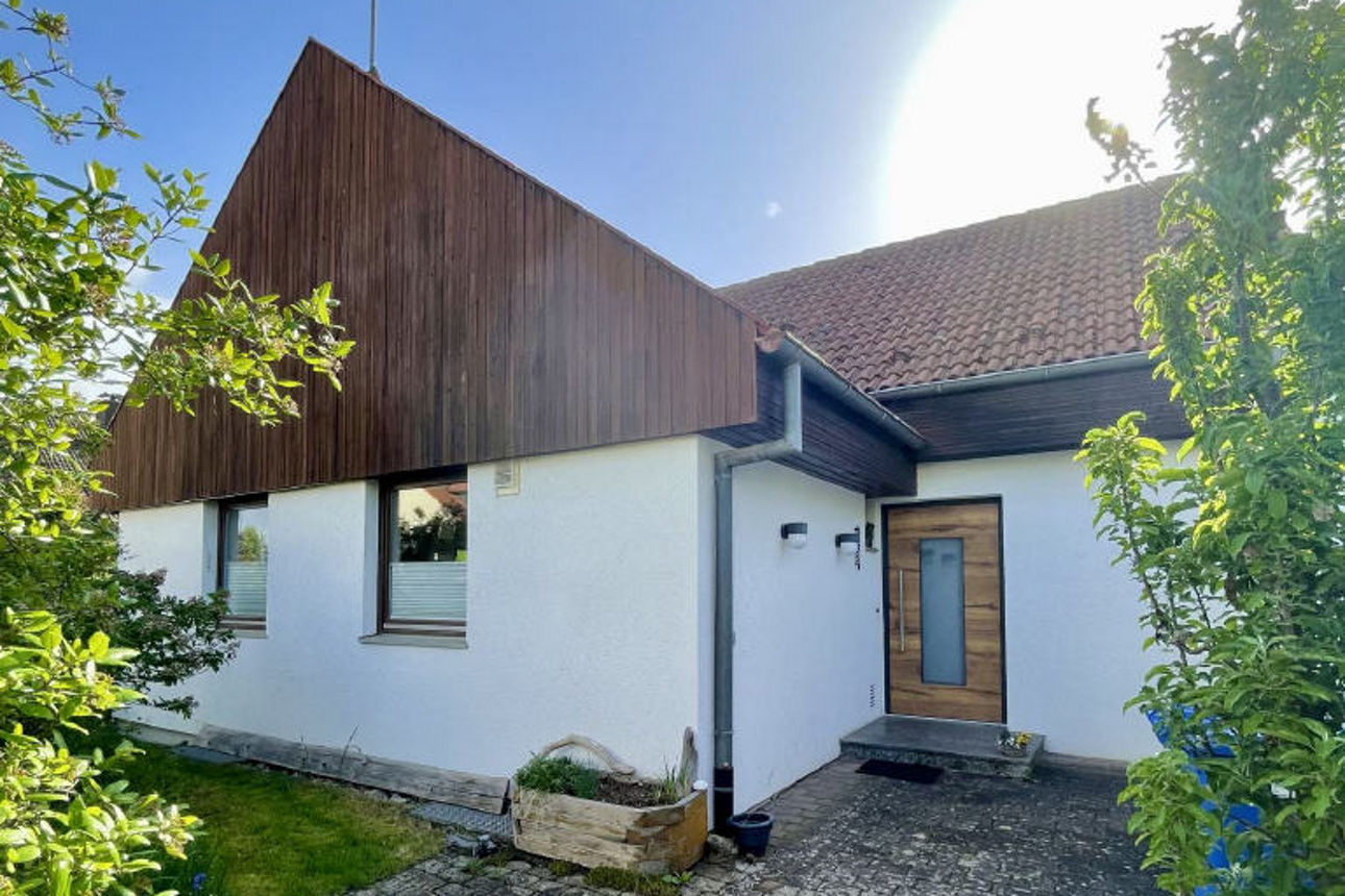 Bild von weißem Einfamilienhaus mit Holzverkleidung an Fassade und gepflastertem Zugangsbereich