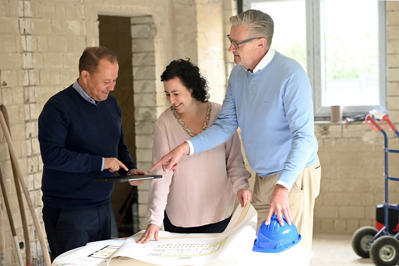 Lächelnde Bankberaterin im Gespräch mit einem Ehepaar im Rohbau