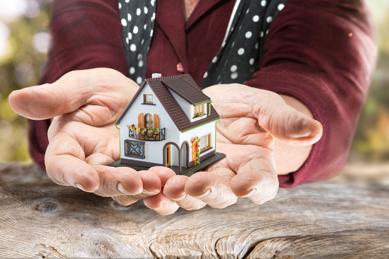 Hände eines älteren Menschen mit Modell eines Hauses