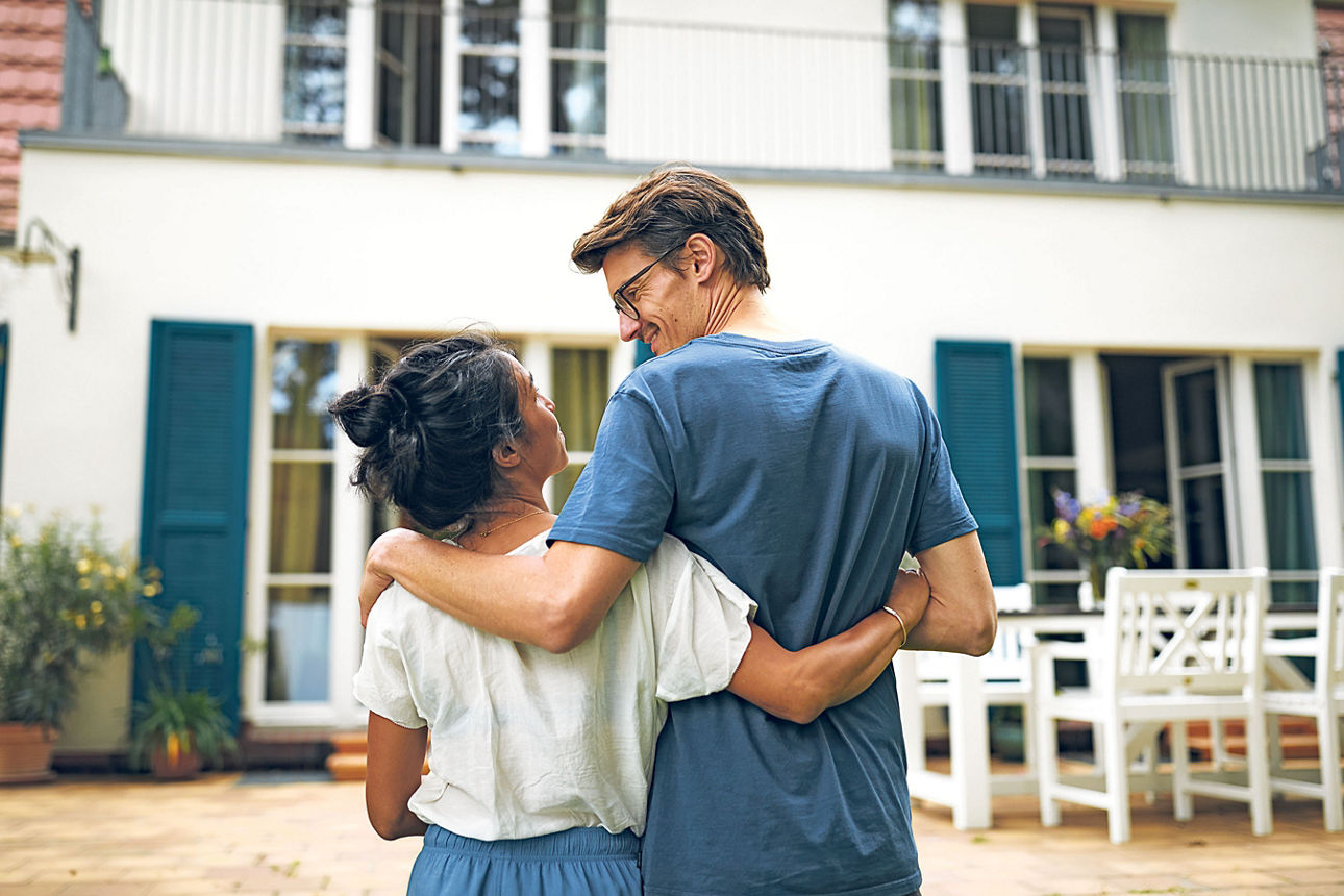 Junges Paar auf der Terrasse vor einem Haus. 