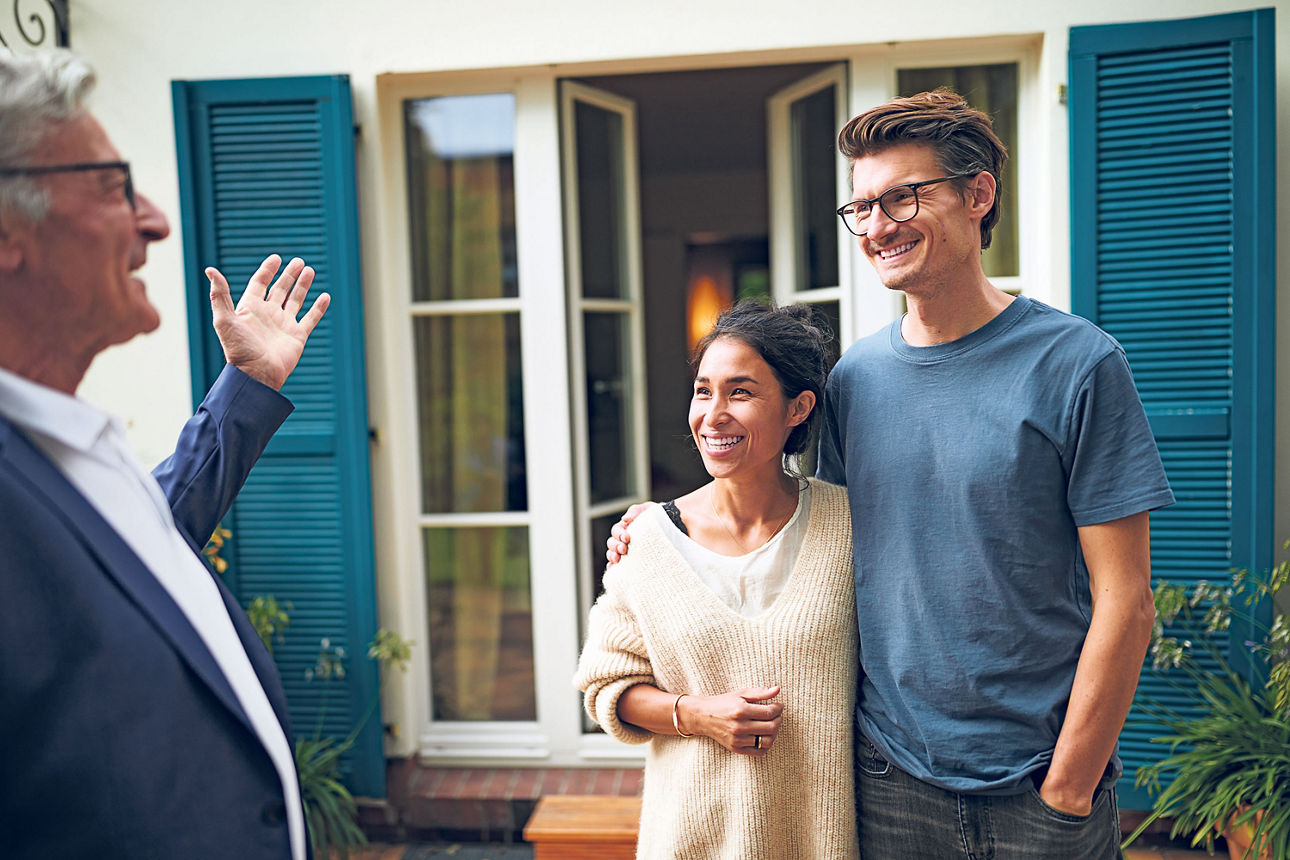 Junges Paar vor offener Terassentür im Gespräch mit älterem Herrn.