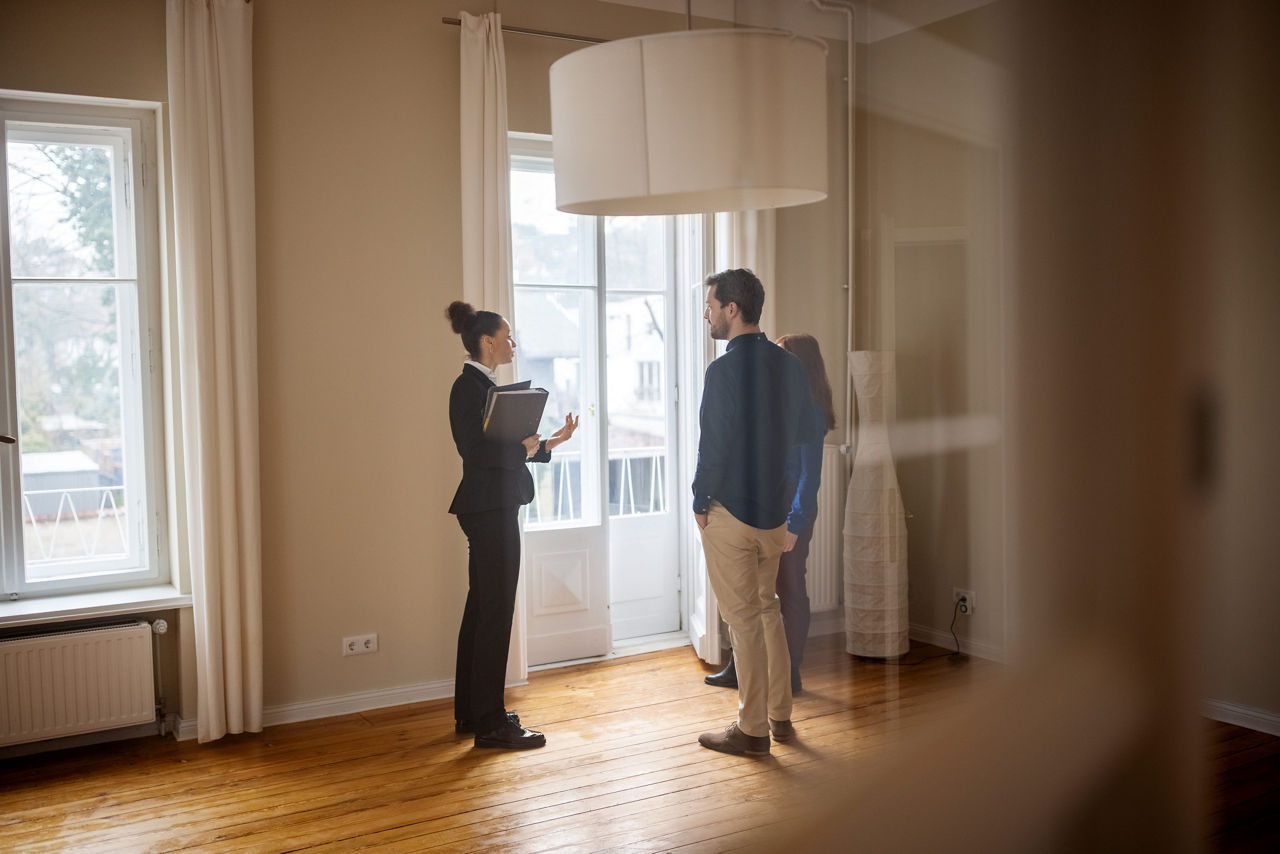 Pärchen steht mit einer jungen Kundenberaterin in einer leeren Wohnung und unterhalten sich darüber die Immobilie zu erwerben