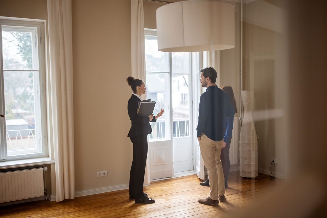 Pärchen steht mit einer jungen Kundenberaterin in einer leeren Wohnung und unterhalten sich darüber die Immobilie zu erwerben