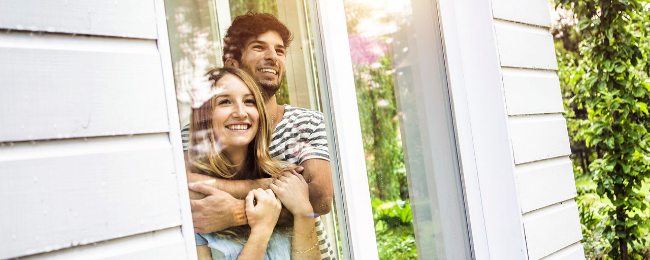 Junges Paar schaut eng umschlungen aus dem Fenster raus