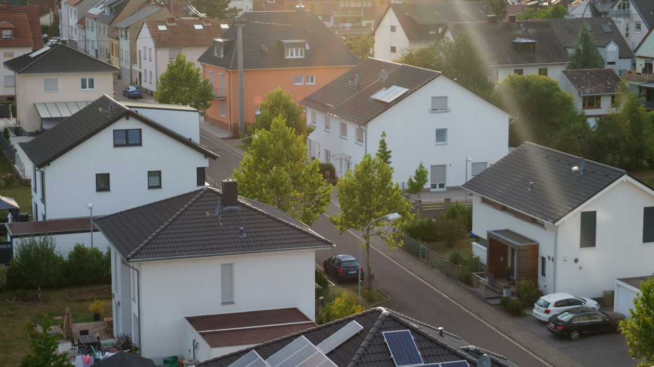 Einfamilienhaussiedlung in einer grünen Wohngegend, mit parkenden Autos entlang der Straße.
