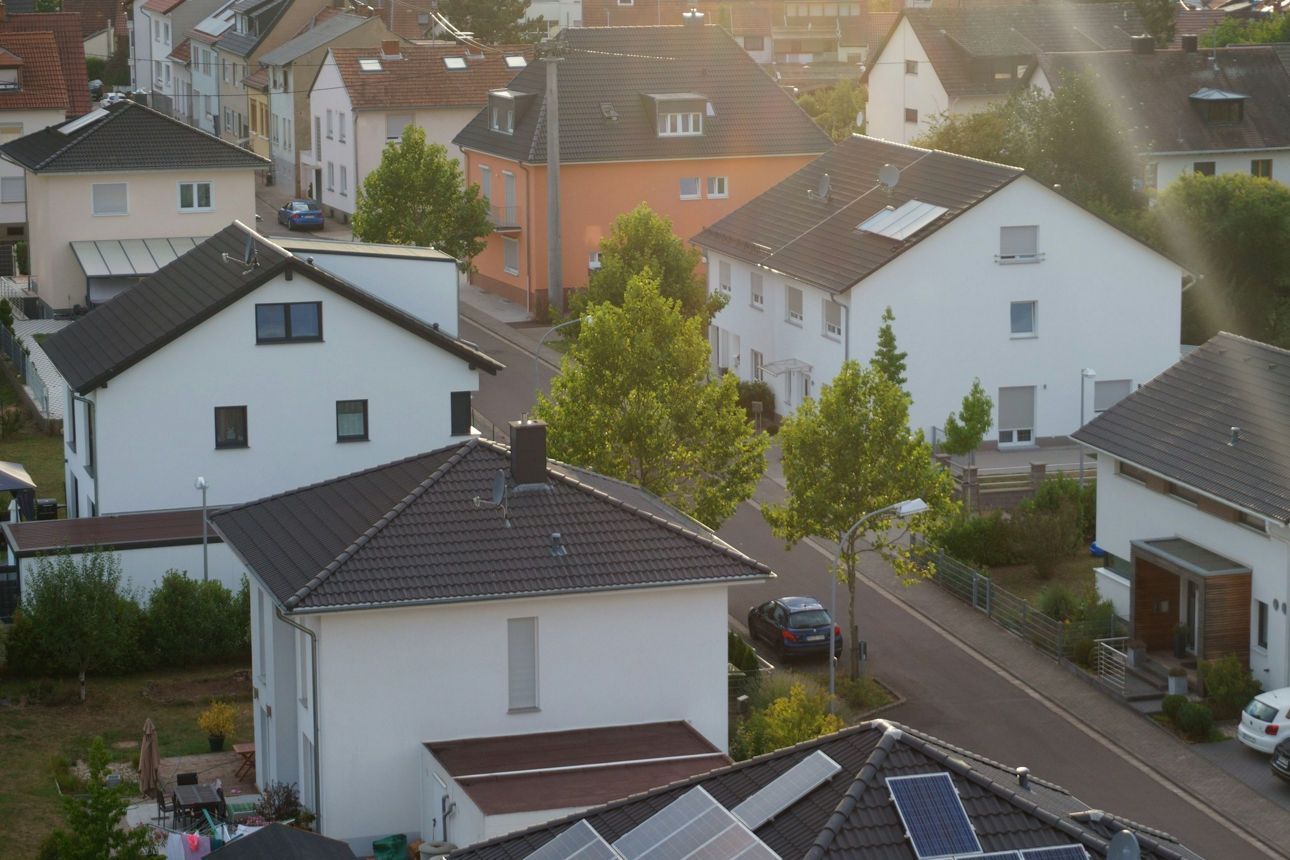 Einfamilienhaussiedlung in einer grünen Wohngegend, mit parkenden Autos entlang der Straße.