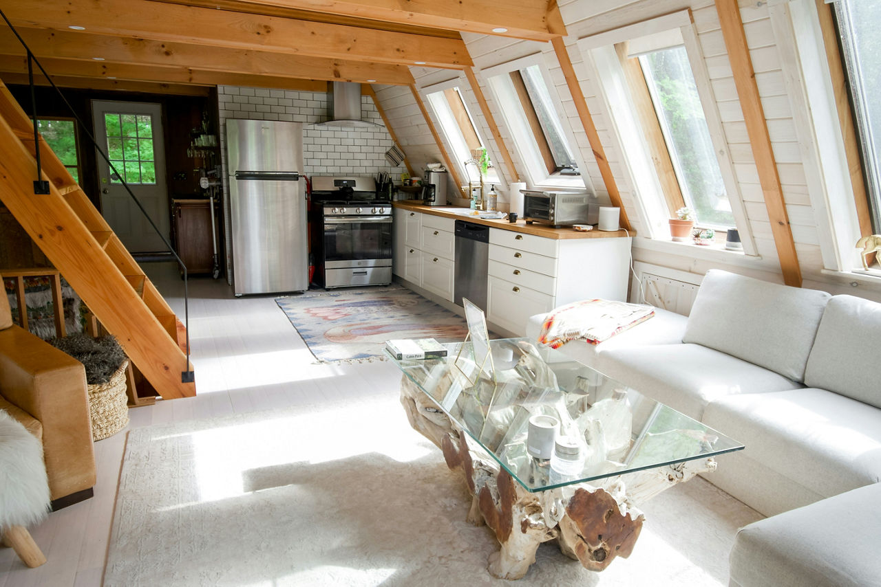 Blick in eine Wohnung mit Holztreppe und Holzbalken, helle Couch und Küche im Hintergrund.