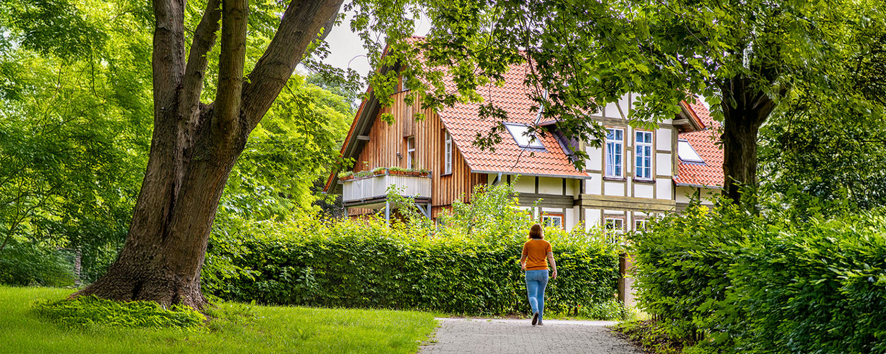 Frau geht im grünen auf ein Haus zu 