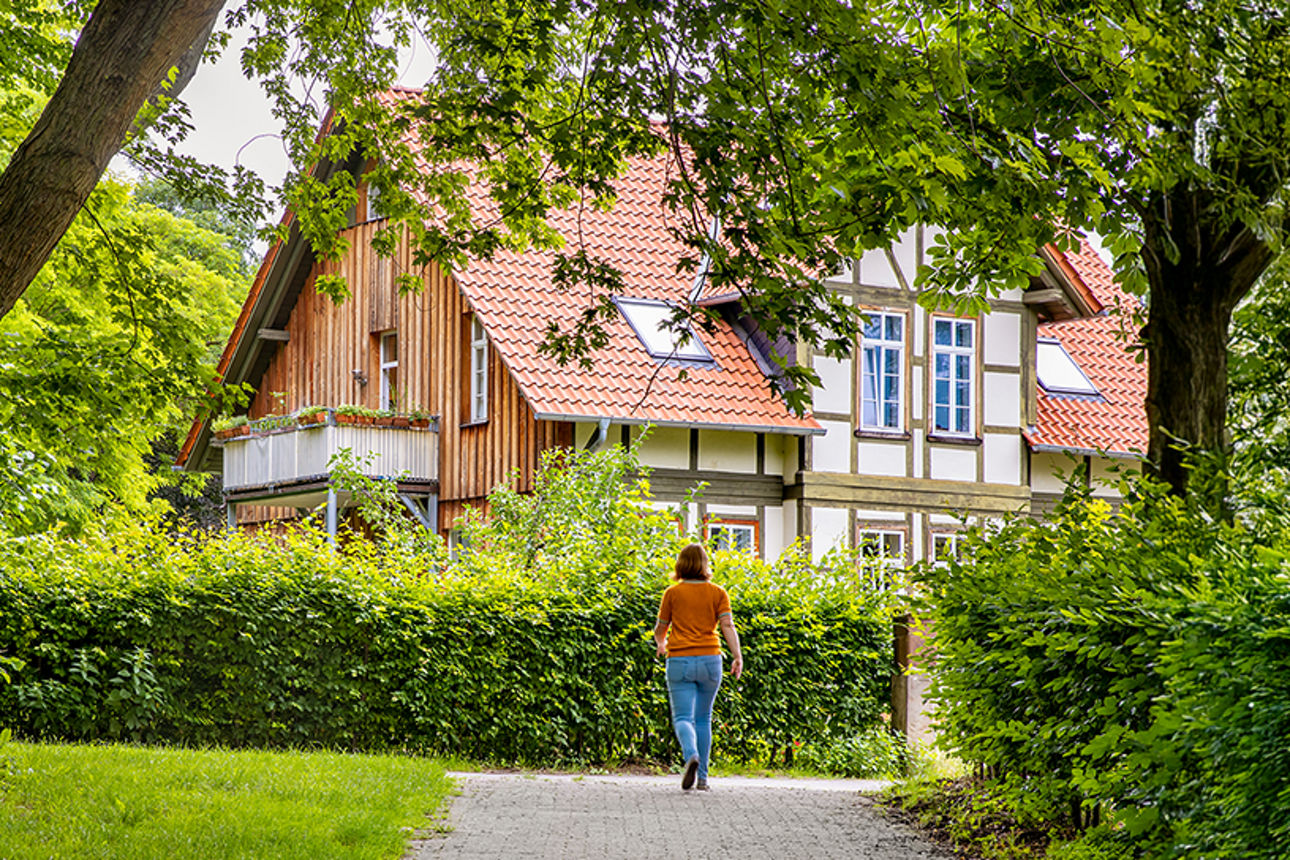 Frau geht im grünen auf ein Haus zu 