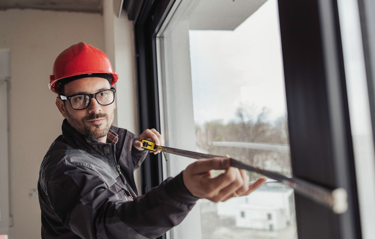 Bauarbeiter misst Fenster mit Maßband im Innenbereich