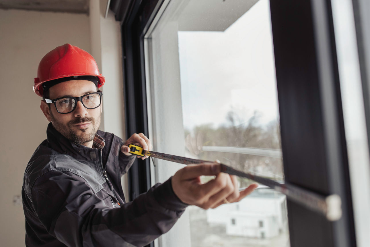 Bauarbeiter misst Fenster mit Maßband im Innenbereich