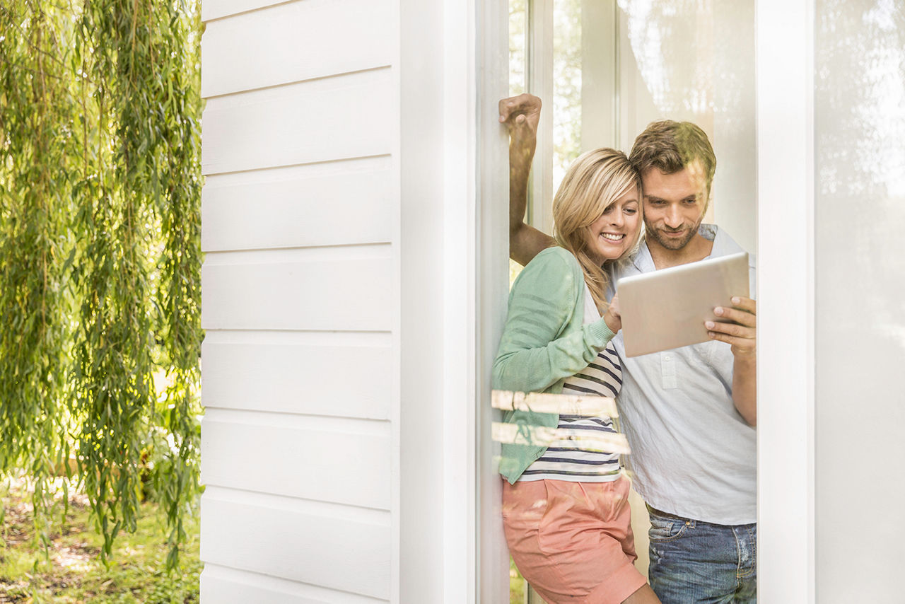 Jungens Paar steht am Fenster und schaut in ein Tablet