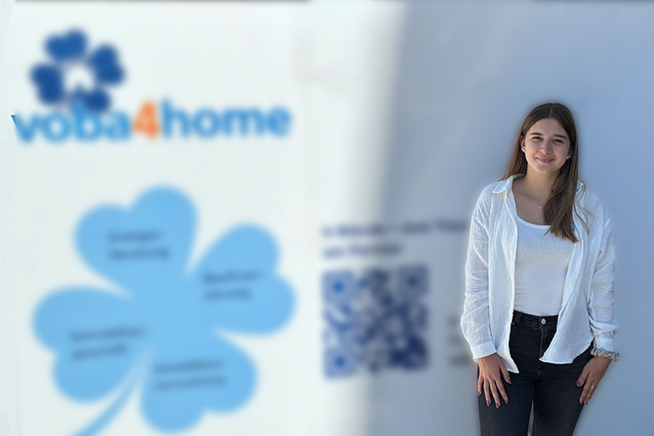Eine Maklerin steht vor einem Banner. Im Hintergrund ist die Marke voba4home sichtbar.