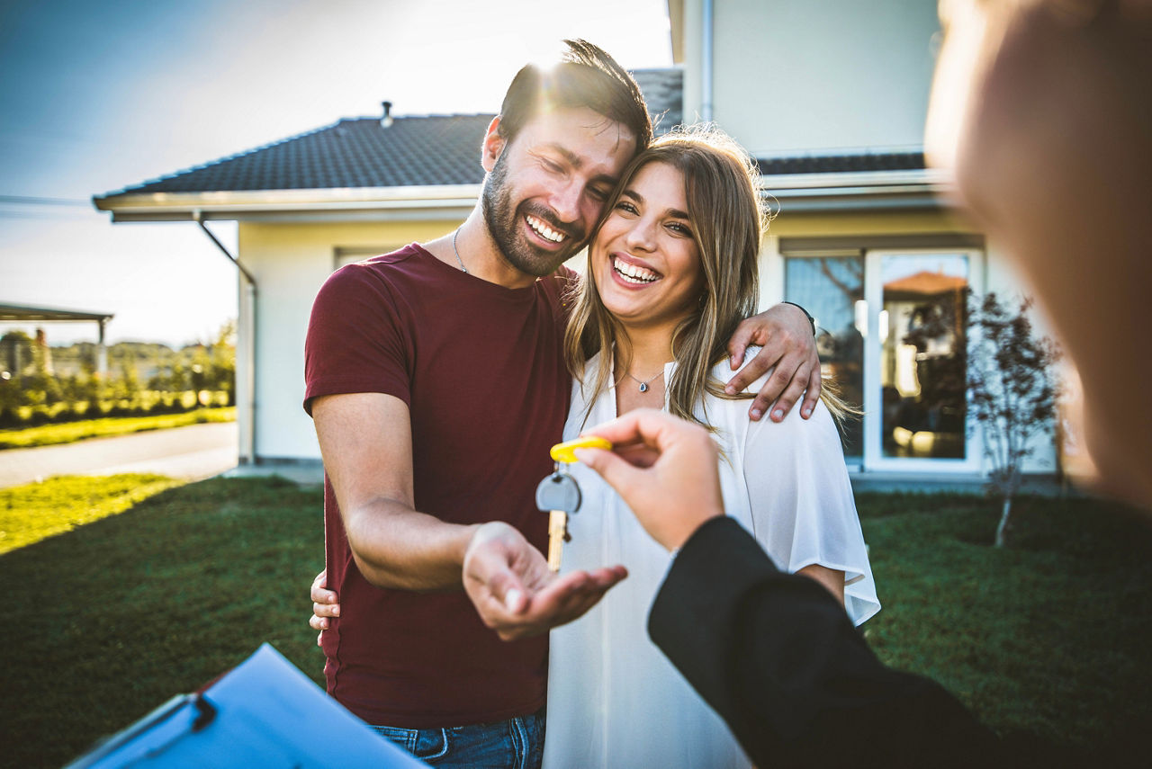 Glückliches Millennial-Paar erhält Schlüssel vom Makler und kauft Immobilien