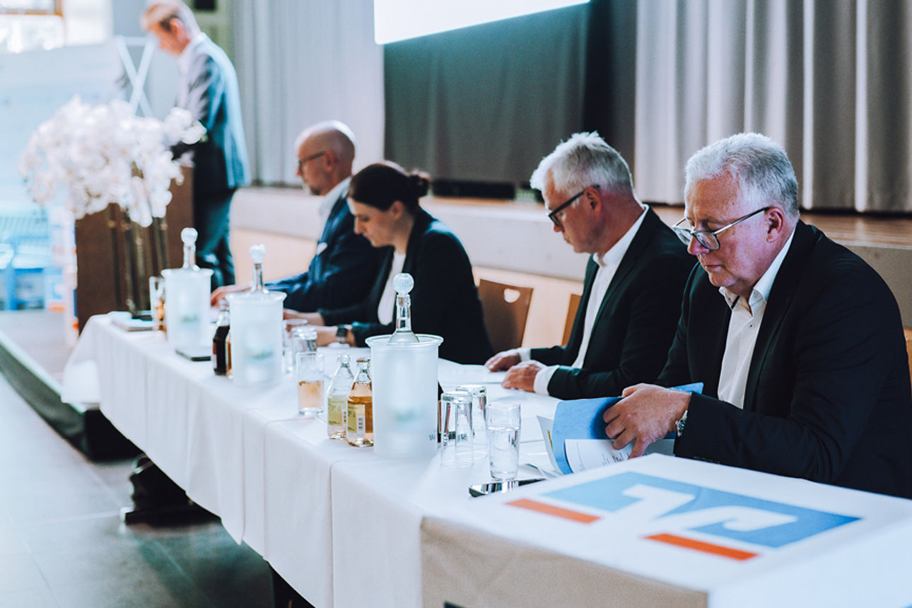 Vier Personen an einem Tisch und eine steht an einem Rednerpult