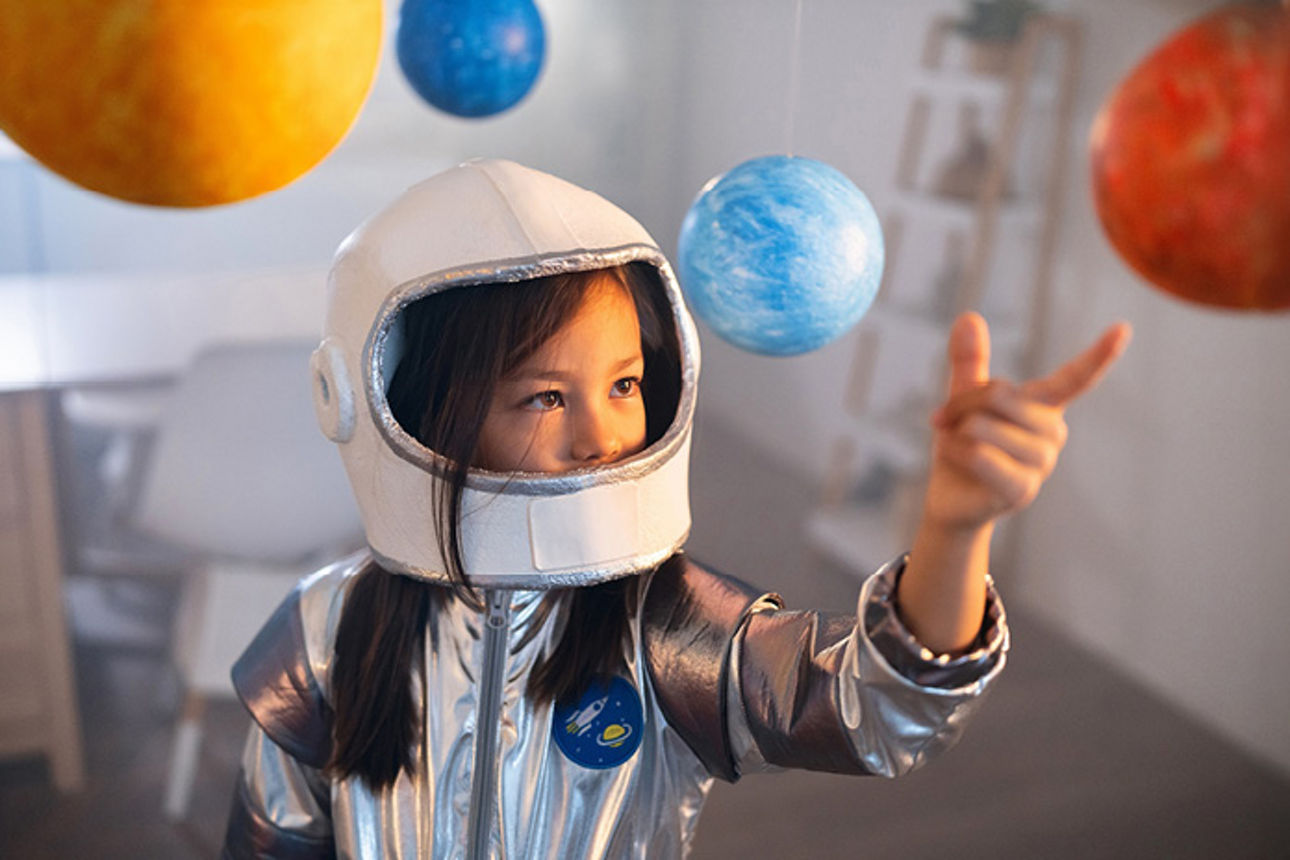Ein junges Mädchen in einem selbstgebauten Astronauten-Anzug umgeben von Planeten