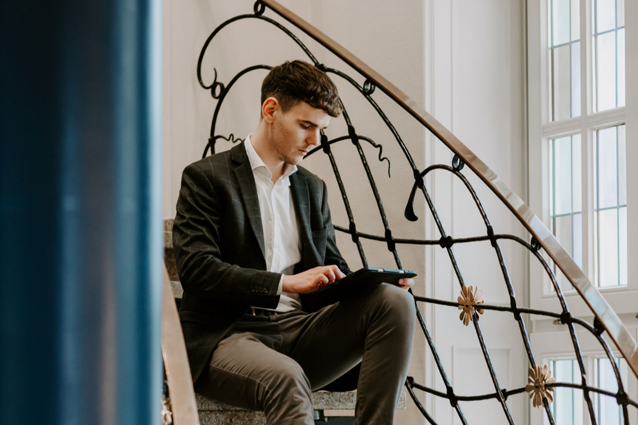 Ein Mann sitzt auf einer Treppe und schaut auf ein Tablet.