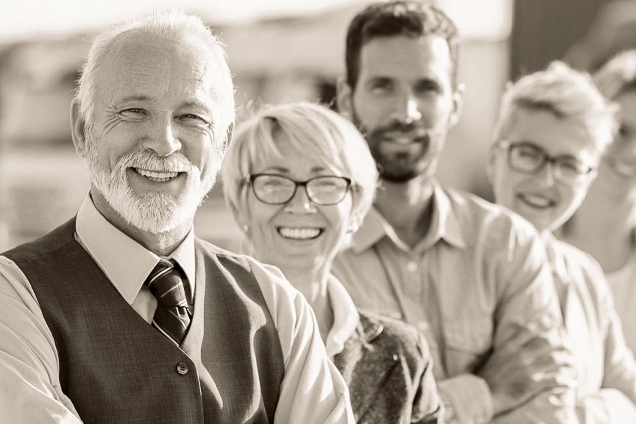 Fünf Personen lächeln, verschränken die Arme und stehen in einer Reihe