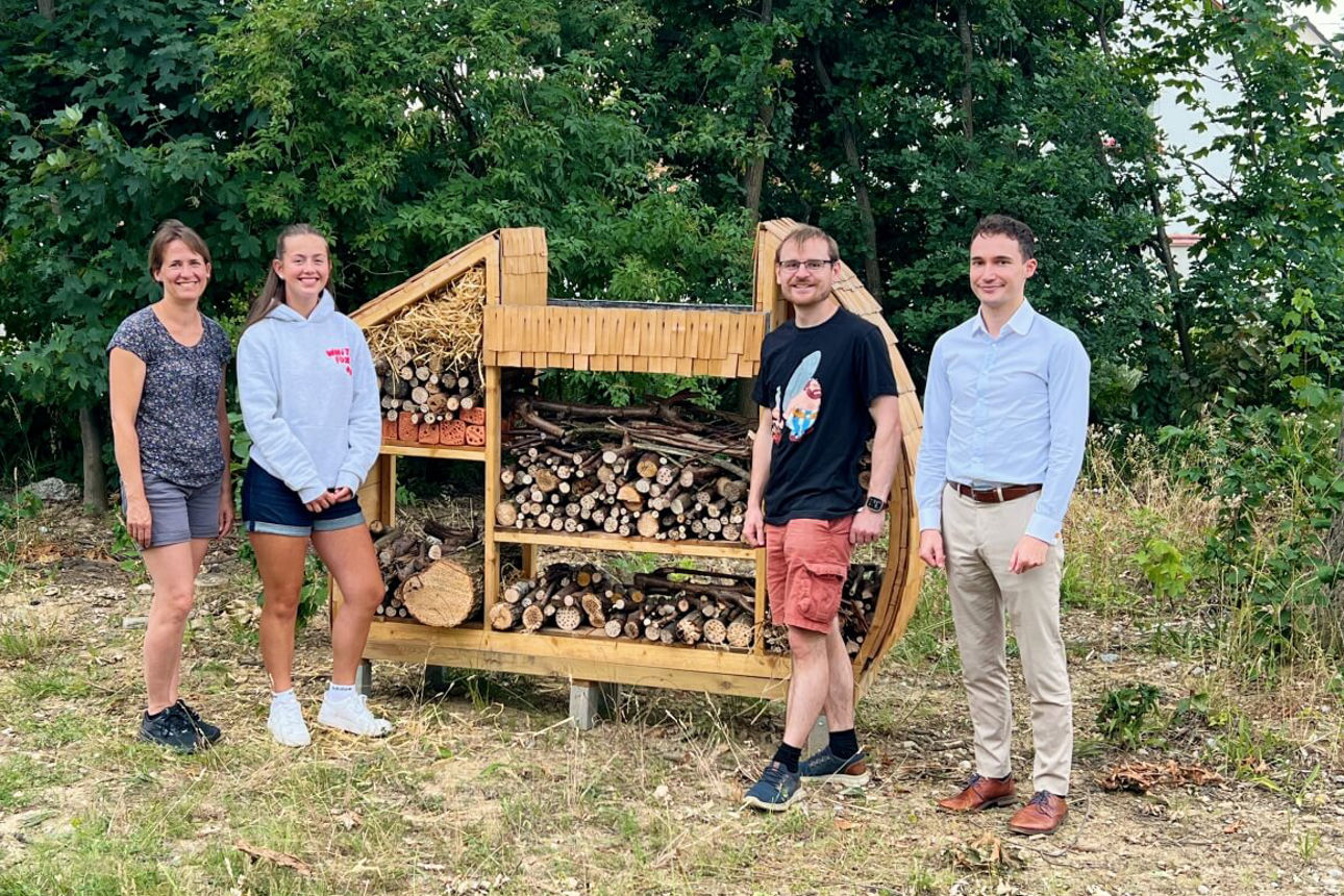 Lehrerin, Schülerin, Lehrer und Vertreter der Bank stehen vor dem fertigen Insektenhotel