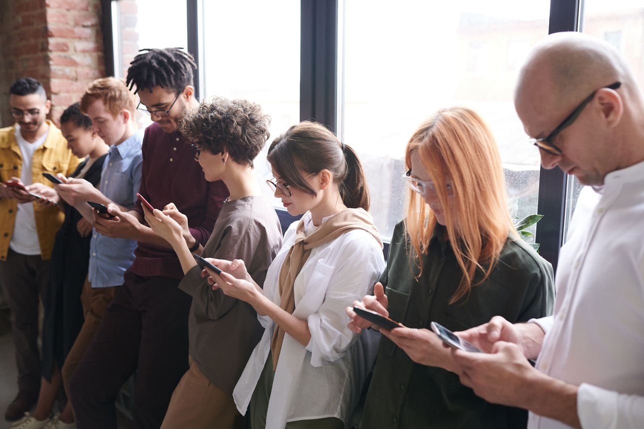 8 Personen stehen in einer Reihe und schauen auf ihre Smartphones