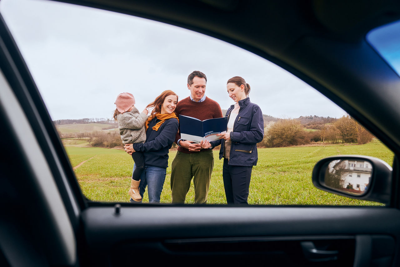 Beraterin steht mit der Familie vor einem Auto und hält eine Mappe in der Hand