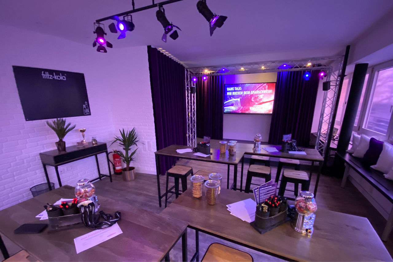 Ein abgedunkelter Workshopraum mit Stehtischen und einem Fernseher.