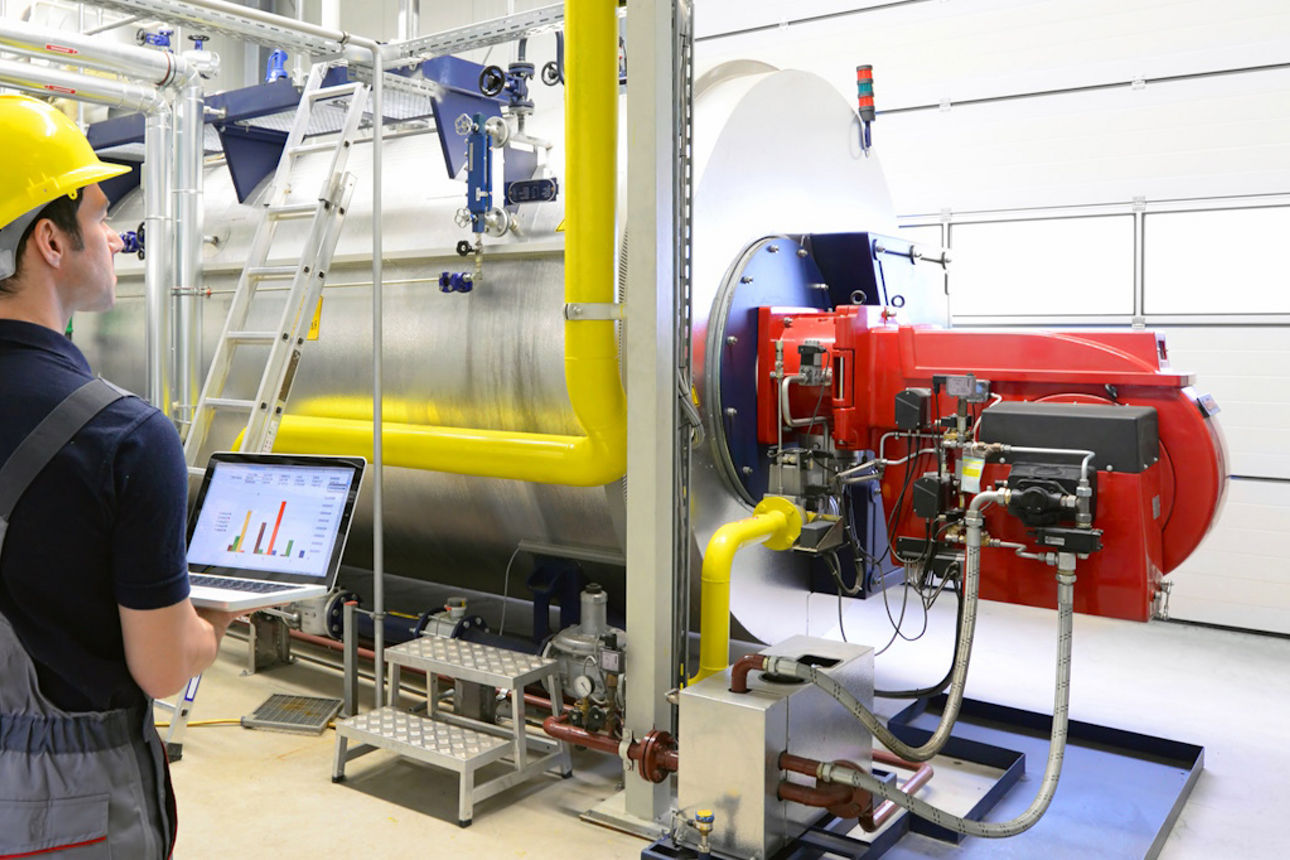 Mann mit Helm steht mit Laptop vor einer Maschine