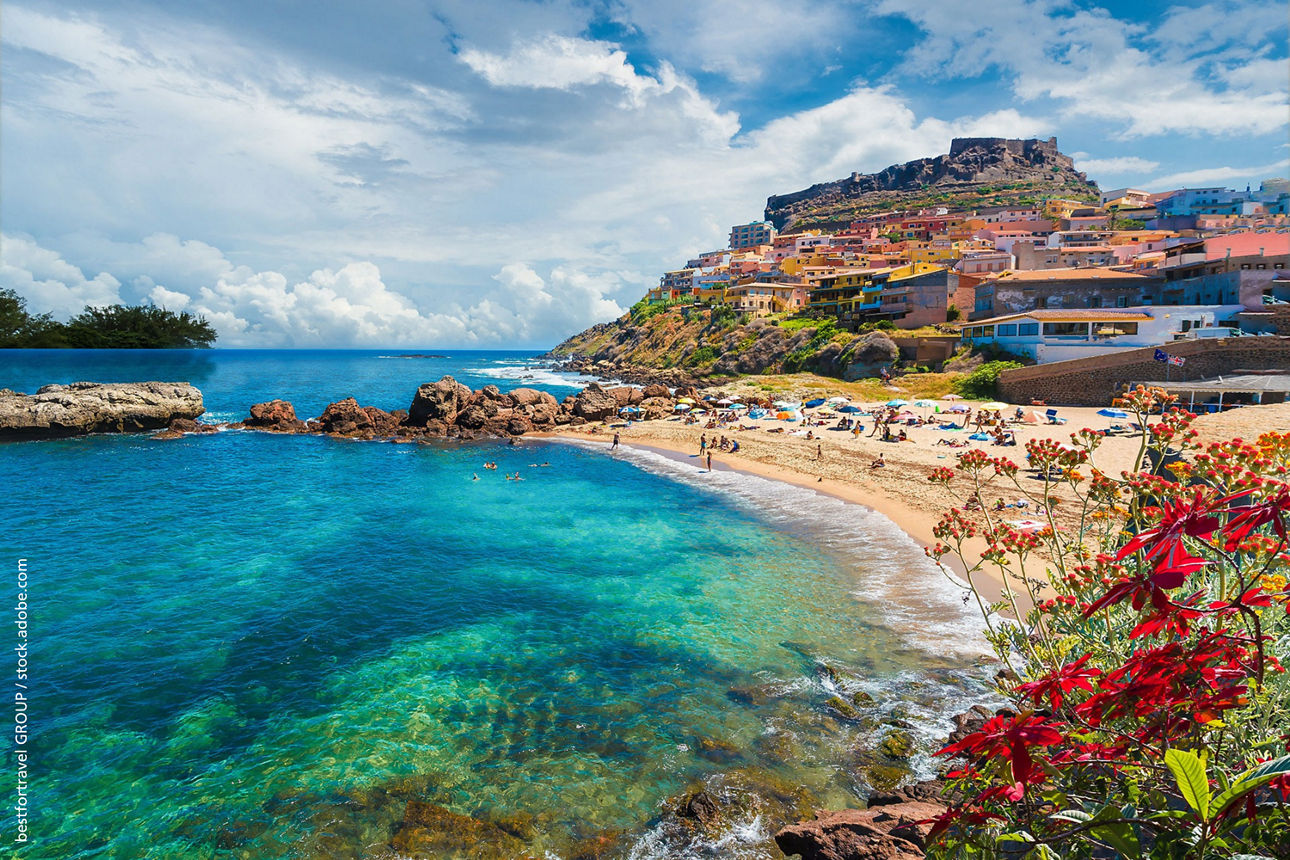 Türkisblaues Meer, ein Sandstrand und bunte Häuser an der sardinischen Küste.