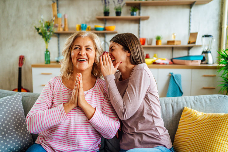 Eine Frau flüstert einer anderen Frau etwas ins Ohr