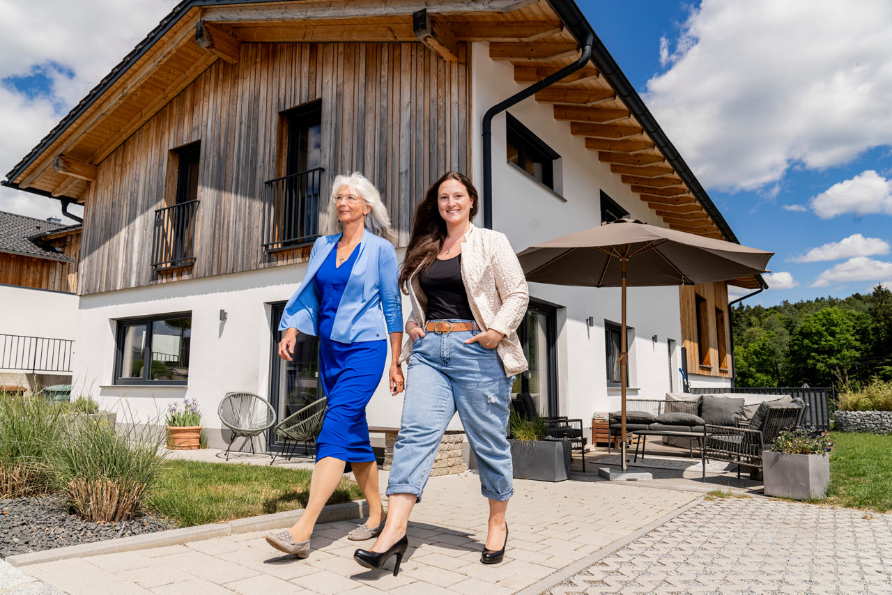 zwei lächelnde Damen gehen von einem modernen Wohnhaus weg
