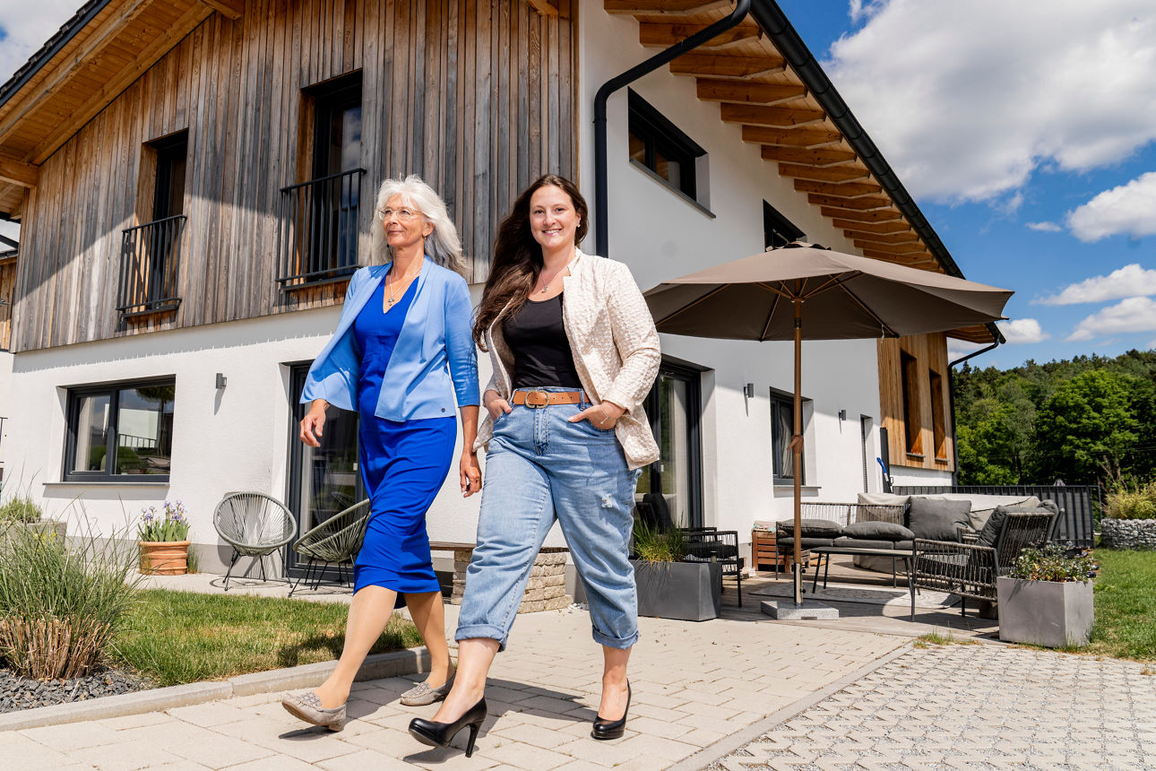 zwei lächelnde Damen gehen von einem modernen Wohnhaus weg