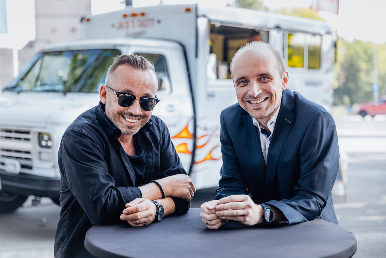 Inhaber Christian Kohl und Bankberater Marco Müller im Gespräch an einem Stehtisch mit Blick auf den Foodtruck von Jack’s Tasty Foodtrucks.