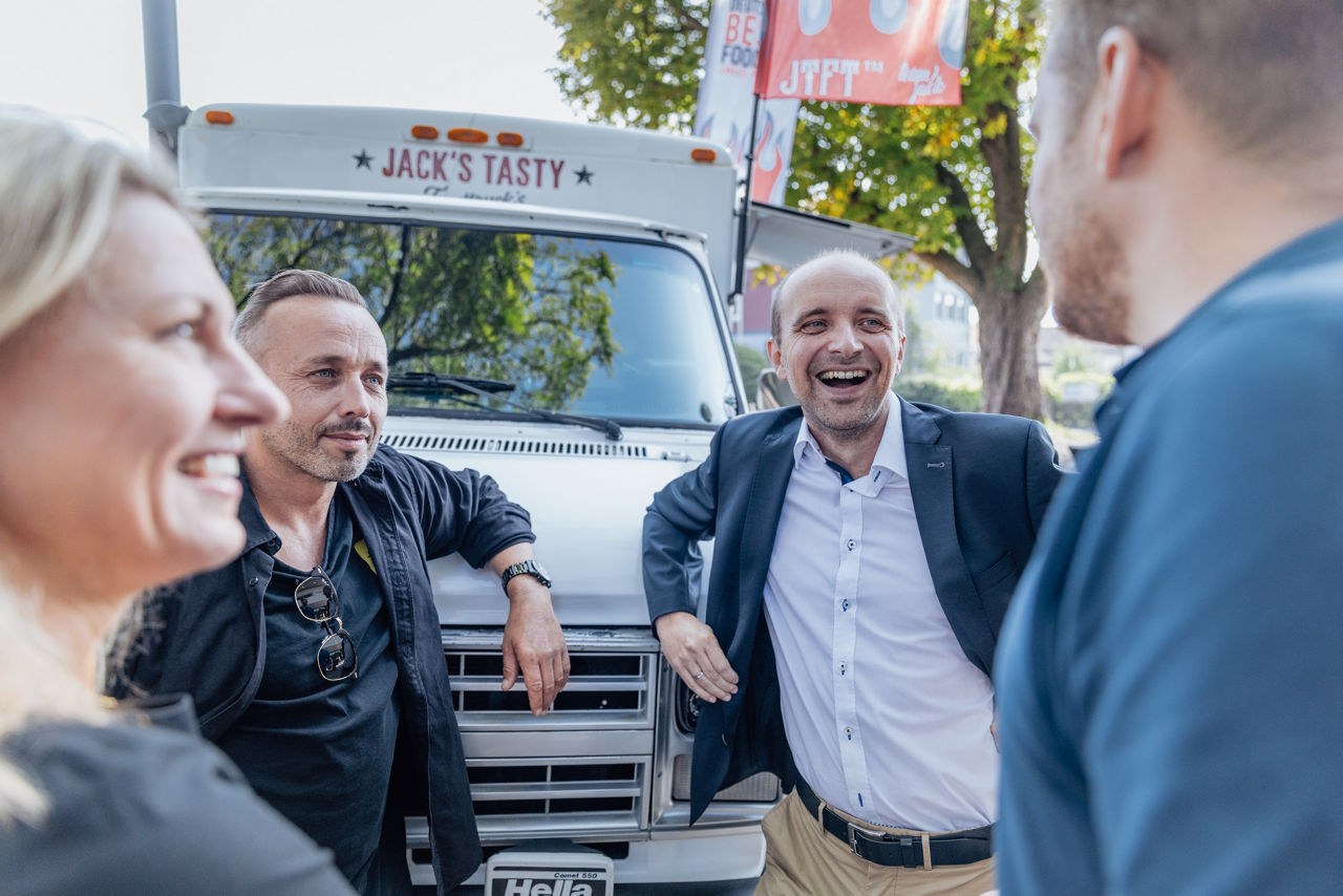Personengruppe im Gespräch vor dem Foodtruck von Jack’s Tasty Foodtrucks während eines Events.