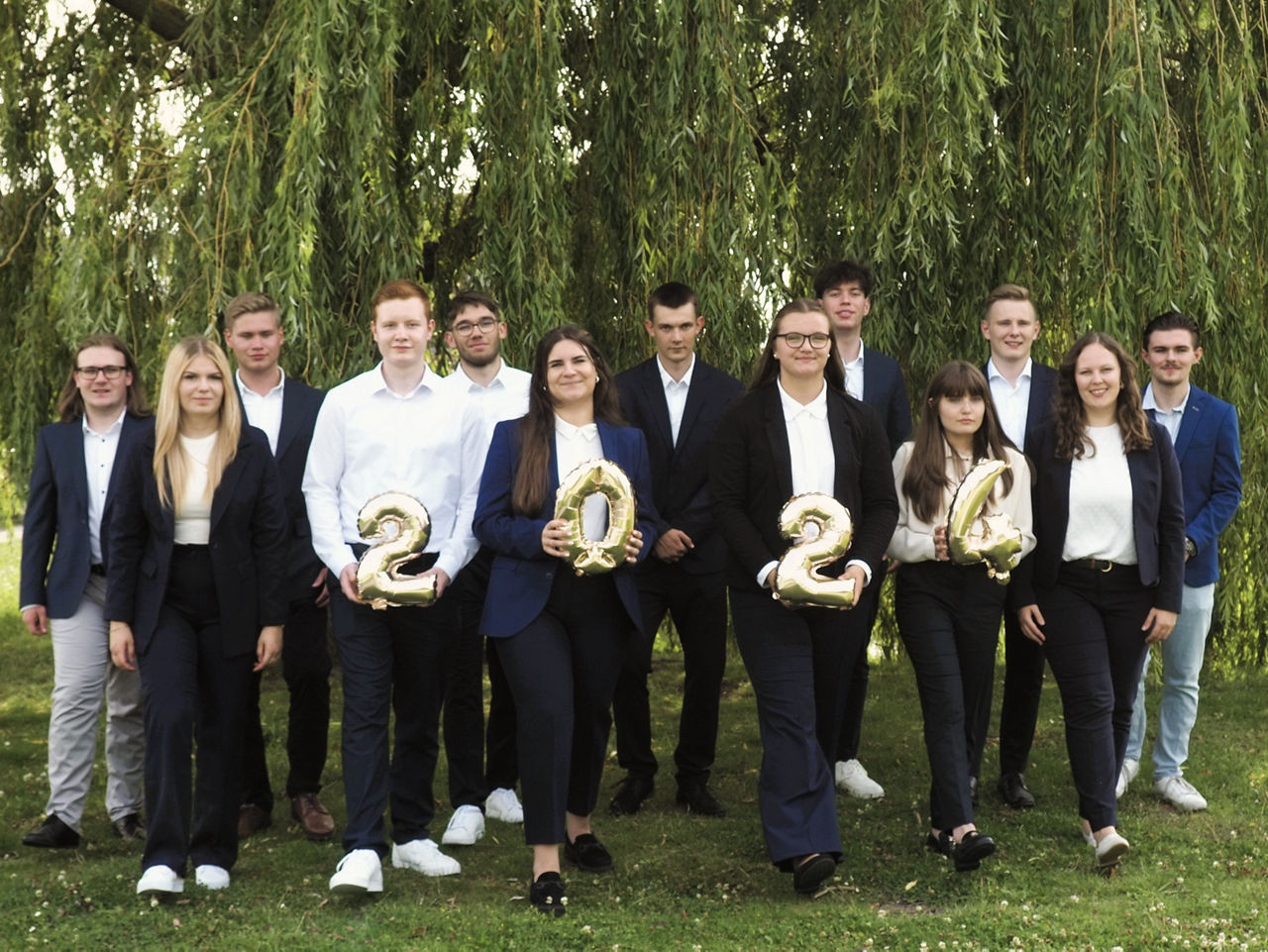 Eine Gruppe mit Azubildenden vor einem grünen Baum.