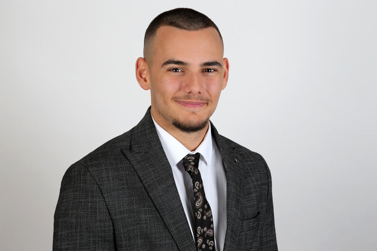 Ein lächelnder Mann in einem Anzug schaut in die Kamera.