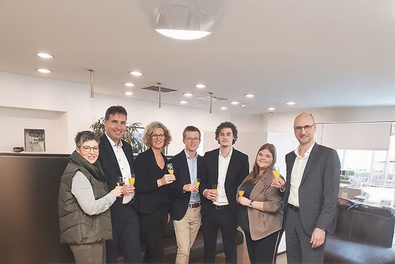 Gruppe von Menschen stoßen gemeinsam an und lächeln dabei in die Kamera