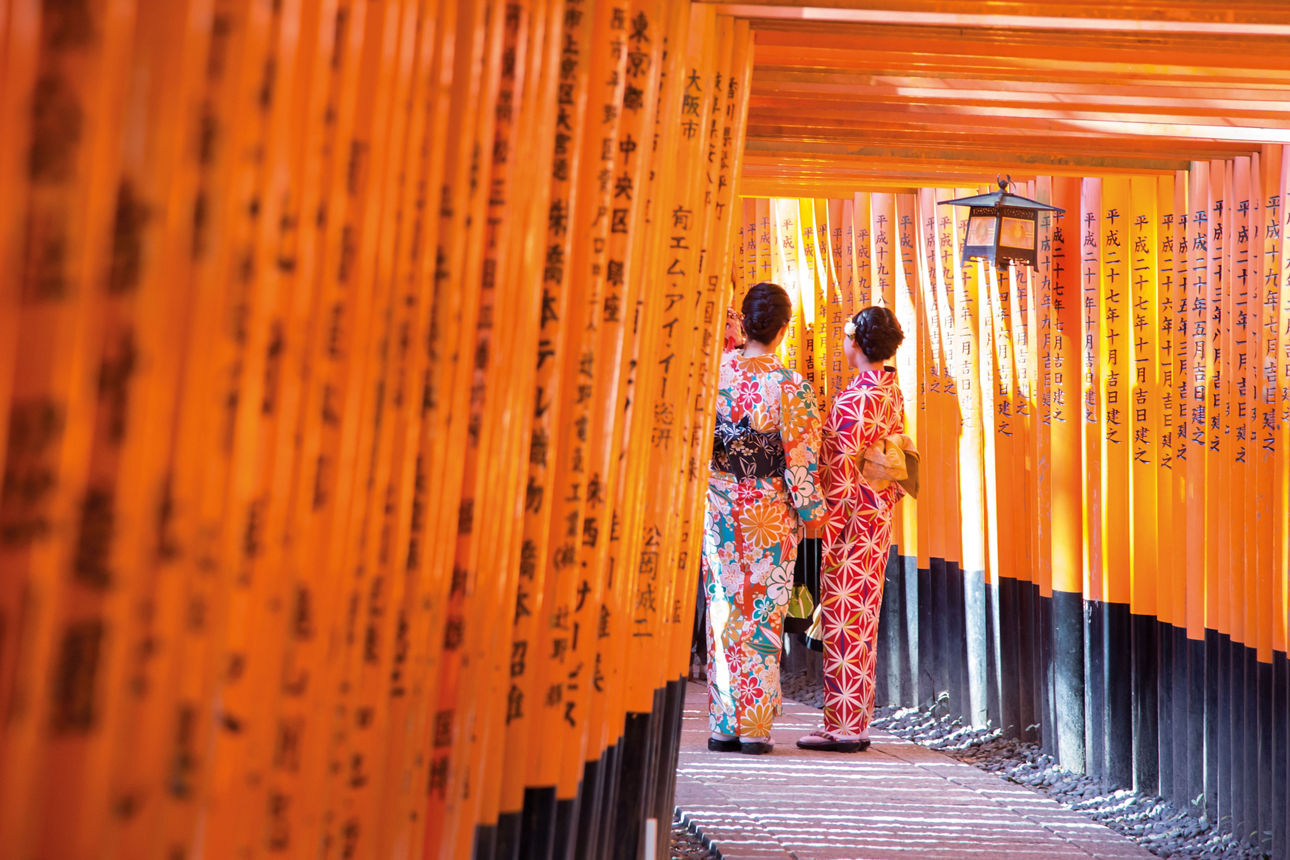 Geishas vor dem roten hölzernen Torii-Tor des Fushimi-Inari-Schreins in Kyoto, Japan.