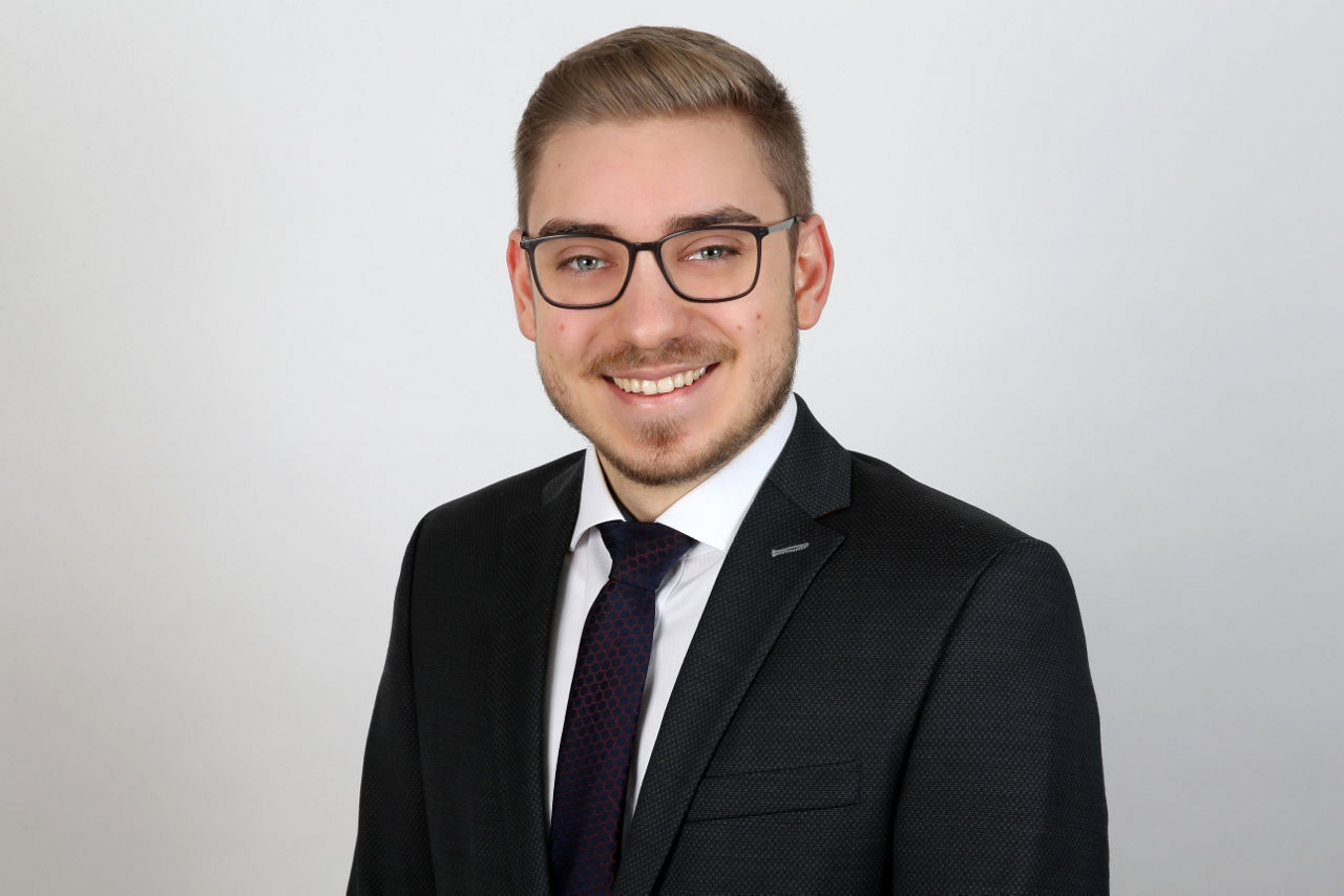 Ein lächelnder Mann in einem Anzug schaut in die Kamera.