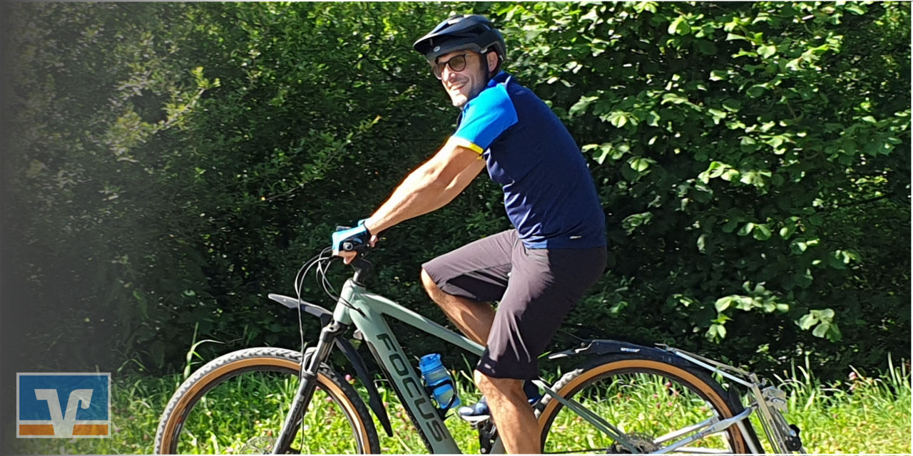 Mann mit Helm fährt bei Sonne auf  Fahrrad durch grünes Waldgelände.