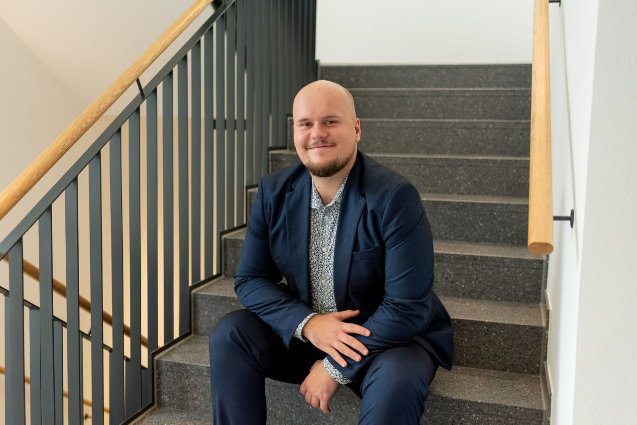 Einzelportrait von Joel Ferati wie er auf einer Treppe sitzt. 