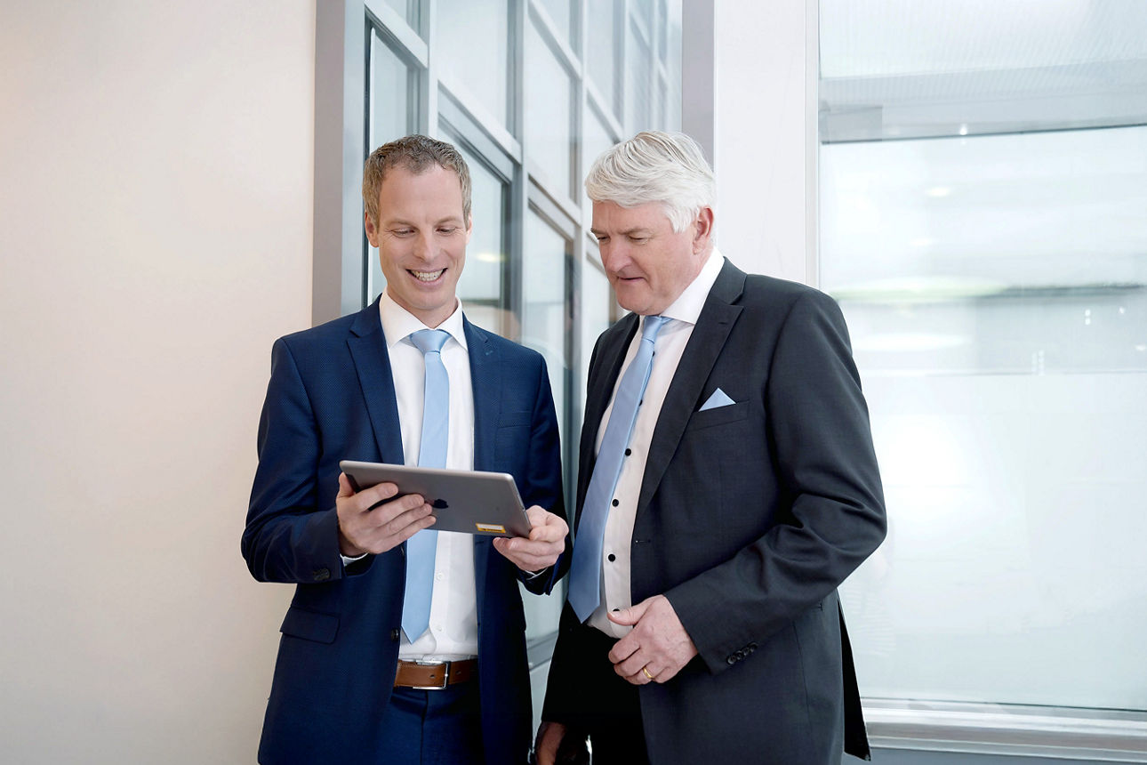 Die Vermögensberater Johannes Sponsel und Hans-Dieter Hübner schauen gemeinsam auf ein Tablet