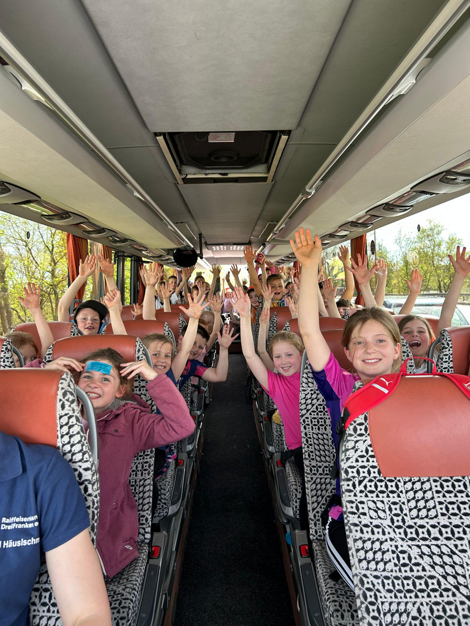 Glückliche Kinder heben die Arme in die Luft in einem Bus.