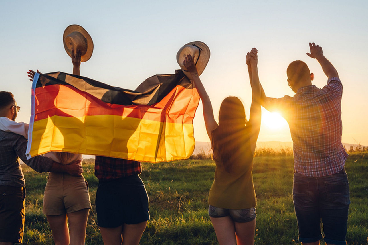fünf Menschen mit Deutschlandfahne laufen Richtung Sonnenuntergang