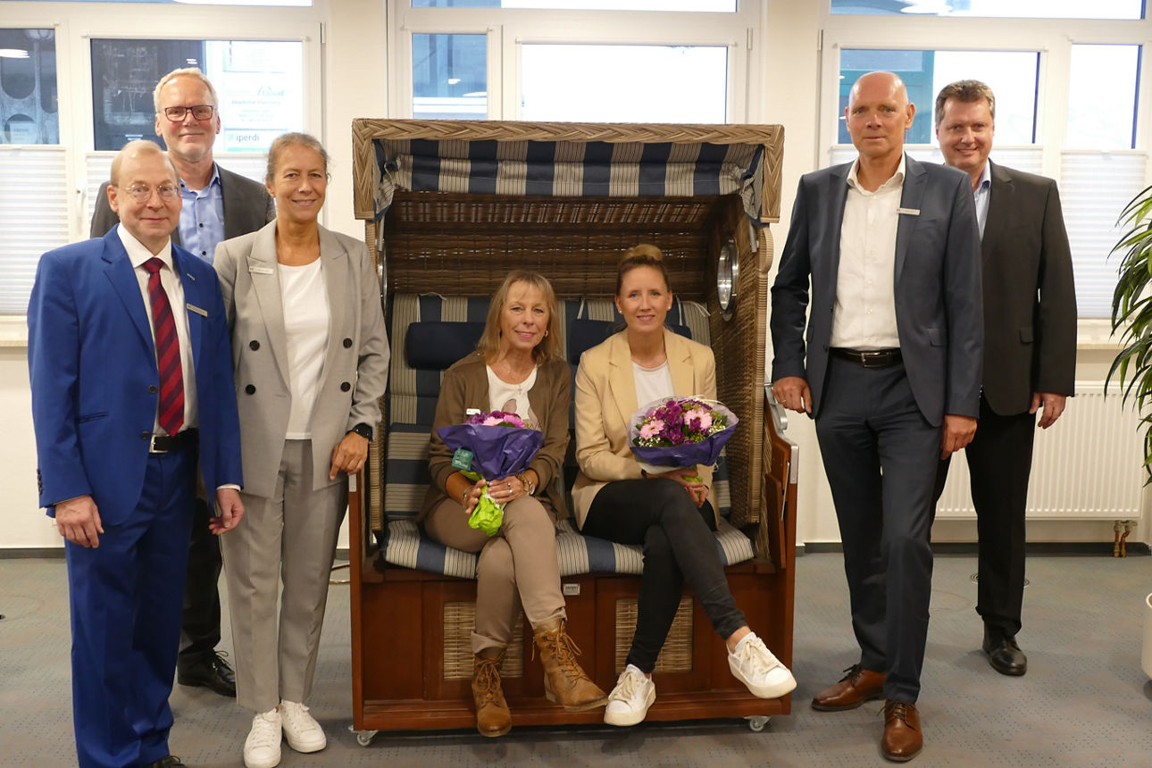 Sieben Personen lächeln in die Kamera, zwei Frauen halten einen Blumenstrauß in der Hand