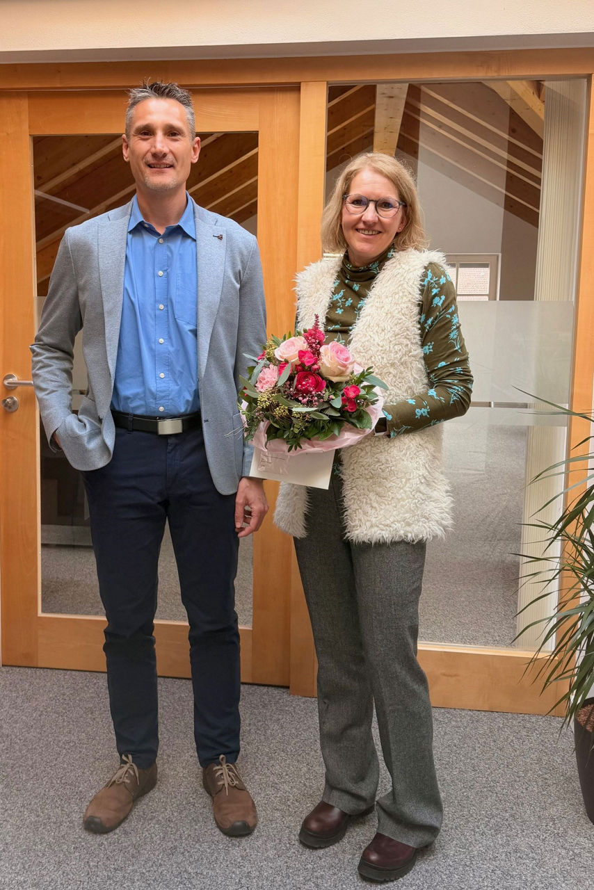 Ein Mann und eine Frau stehen nebeneinander, die Frau hält einen Blumenstrauß in den Händen, beide lächeln in die Kamera